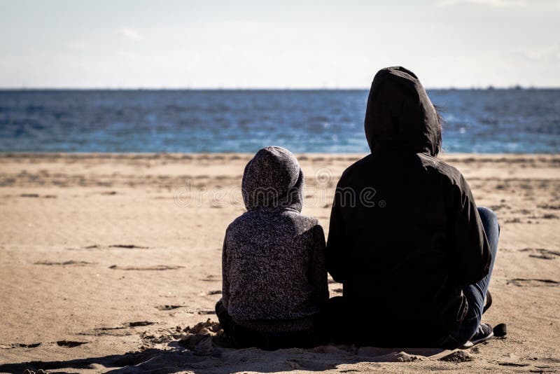 Son and mother sitting turn back on the beach and looking at the sea