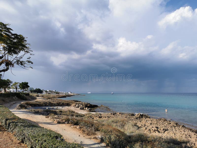 Sonnenküste des Mittelmeers mit Bäumen und Steinen dramatischen Himmel und Regen über dem Meer Boote im Meer und die größte lizenzfreie stockfotografie