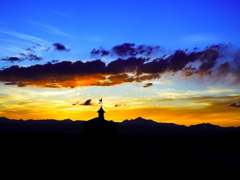 Bright sunset over rocky mountains and barn with weather vain rooster silhouette. Bright sunset over rocky mountains and barn with weather vain rooster silhouette