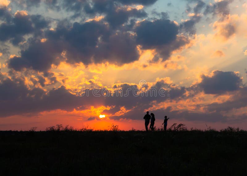 Sonnenuntergangdämmerungs-Sonnenstrahlen über Feldhimmel fangen die Familie auf, die nahe der Sonne auf dem Horizontschattenbild stockbild Sonnenuntergangdämmerungs-Sonnenstrahlen über Feldhimmel fangen die Familie auf, die nahe der Sonne auf dem Horizontschattenbild stockbild