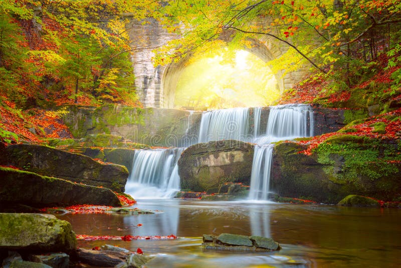 Sonniger Herbstlandschaftsflusswasserfall im bunten Herbstwald mit alter Brücke lizenzfreies stockfoto