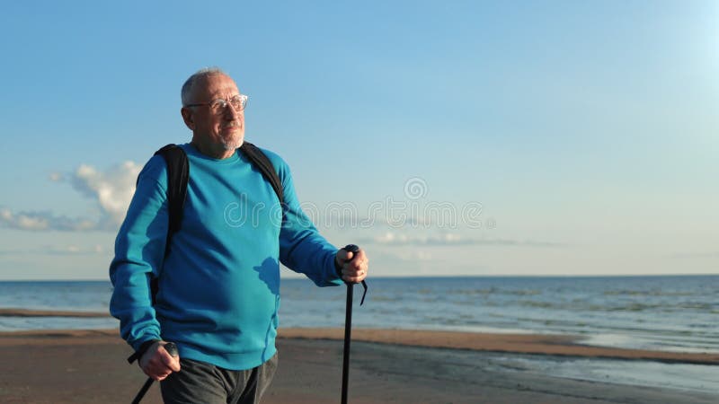 Sonriente activo anciano hombre escandinavo bastón de caminar cardio ejercicio deportivo en playa de arena soleada mar