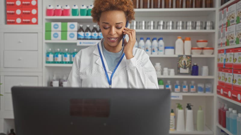 Sonriente farmacéutica afroamericana consultando por teléfono en farmacia foto de archivo libre de regalías