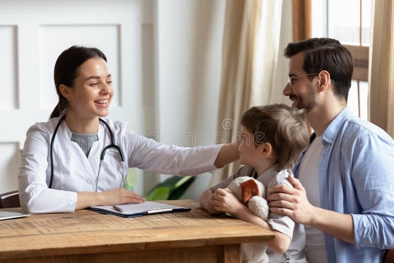 Sonriente joven y agradable doctora acariciando cabeza de paciente pequeño. foto de archivo