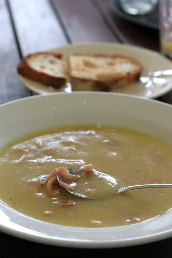 Close up of spoon in bowl of potato, leek and bacon soup with bread in background. Close up of spoon in bowl of potato, leek and bacon soup with bread in background