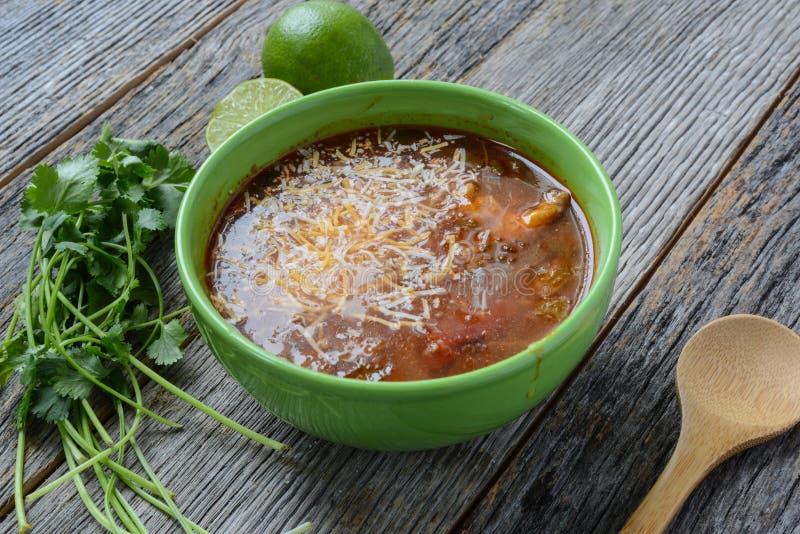 Tortilla Soup with Cheese, Lime, Cilantro and Wooden Spoon on Rustic Wood Background. Tortilla Soup with Cheese, Lime, Cilantro and Wooden Spoon on Rustic Wood Background