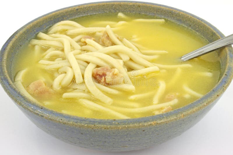 A close view of a serving of chicken noodle soup in a stoneware dish with spoon. A close view of a serving of chicken noodle soup in a stoneware dish with spoon.