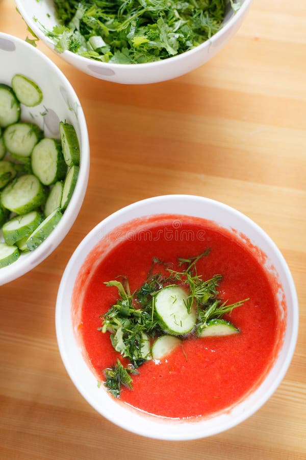 Sopa deliciosa del tomate con las especias aromáticas y los pepinos orgánicos en un cuenco blanco en una tabla de madera fotos de archivo Sopa deliciosa del tomate con las especias aromáticas y los pepinos orgánicos en un cuenco blanco en una tabla de madera fotos de archivo