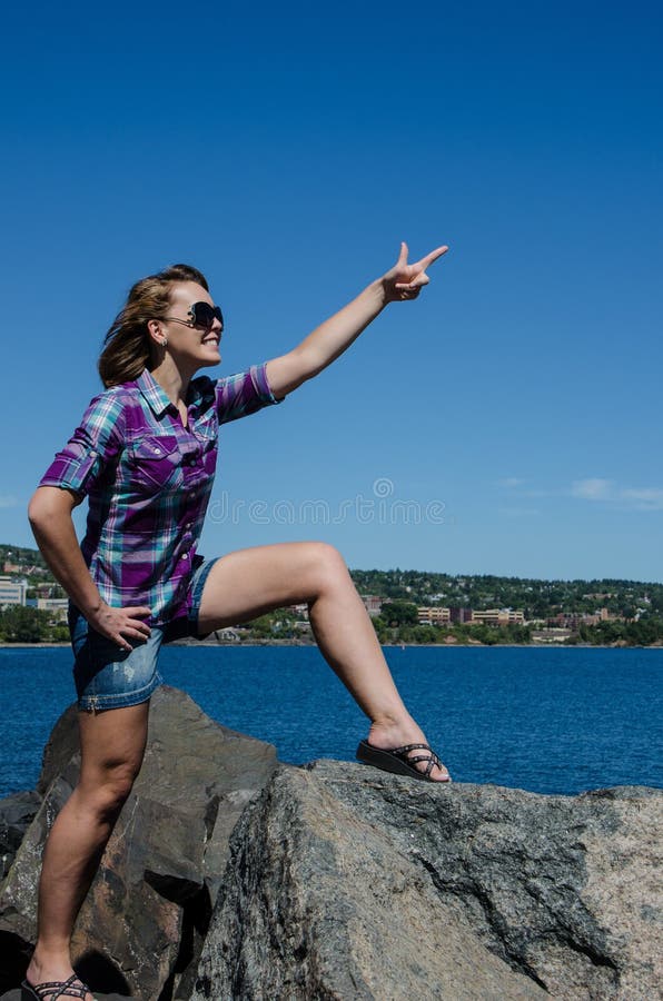 Soportes hermosos de la mujer adulta encima de rocas con los brazos que señalan fotografía de archivo Soportes hermosos de la mujer adulta encima de rocas con los brazos que señalan fotografía de archivo