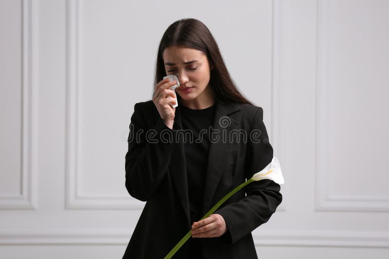 Sorglig kvinna med blomkorgsbefruktning nära vit vägg. begravningsceremoni royaltyfria foton