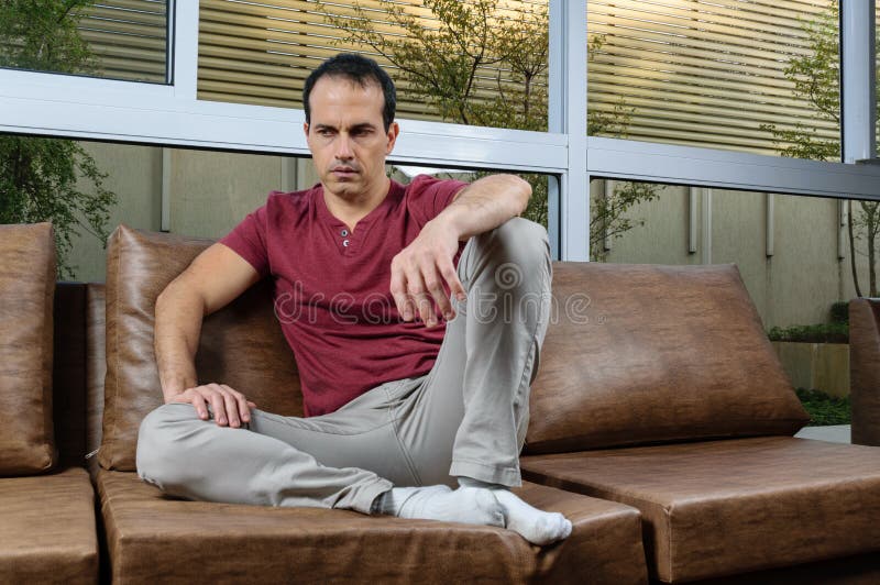 44-year-old man in a photo session on the brown sofa, doing various poses, joy, serious, sadness, with smartphone in hand and staring at the camera. 44-year-old man in a photo session on the brown sofa, doing various poses, joy, serious, sadness, with smartphone in hand and staring at the camera.