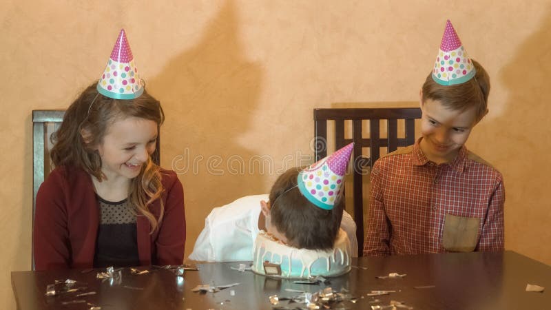 Sorglose Kinder an einer Geburtstagsfeier Junge eingetauchtes Gesicht im Geburtstagskuchen Familienfeierkonzept lizenzfreie stockfotografie