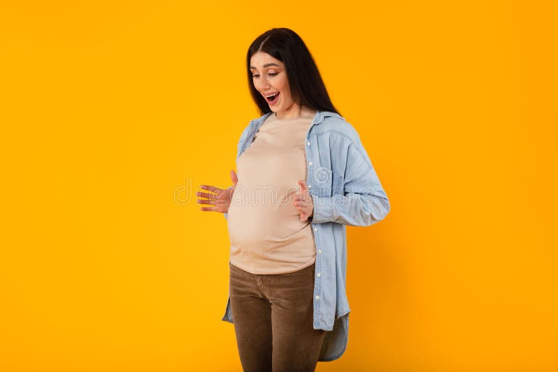 Sorprendida joven embarazada que siente patadas de bebé dentro del vientre reaccionando emocionalmente a la próxima maternidad foto de archivo