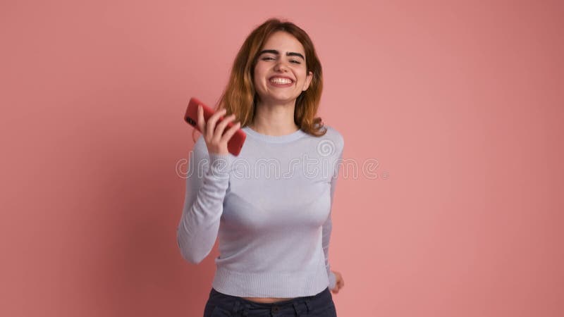 Sorprendida joven pelirroja usando teléfono móvil con antecedentes rosas almacen de video