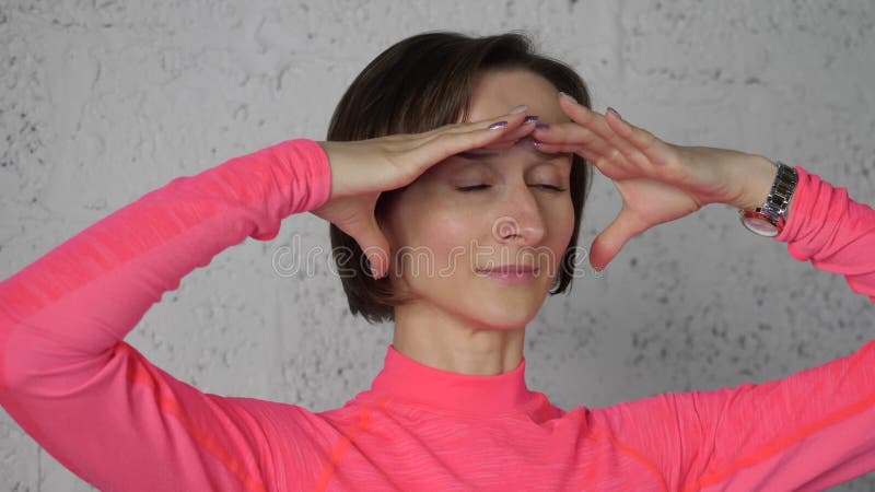 Sorprendida mujer mirando lejos y sosteniendo palmas en la frente mientras se enfrenta al yoga. Joven haciendo gimnasia facial en