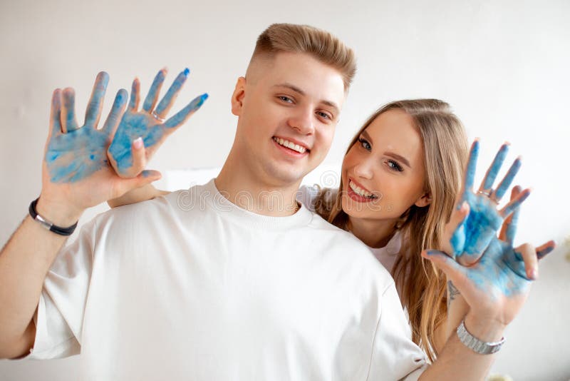 Sorridente felice giovane coppia di belle donne dietro l'uomo in camicie bianche con le mani ricoperte di vernice blu. immagini stock