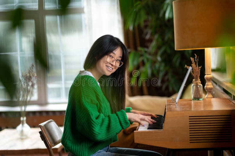 Sorridente garota asiática sentada perto do piano em casa fotos de stock royalty free