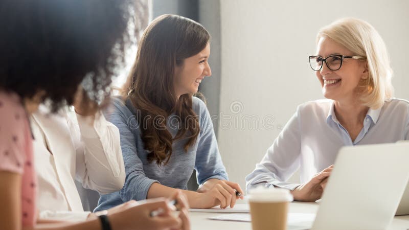 Sorridere amichevole donne di affari anziane e giovani che parlano ridendo della riunione immagine stock libera da diritti Sorridere amichevole donne di affari anziane e giovani che parlano ridendo della riunione immagine stock libera da diritti