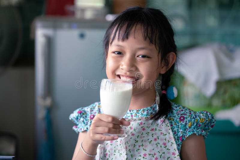 Sorridi bambina asiatica che regge un bicchiere di latte immagine stock libera da diritti