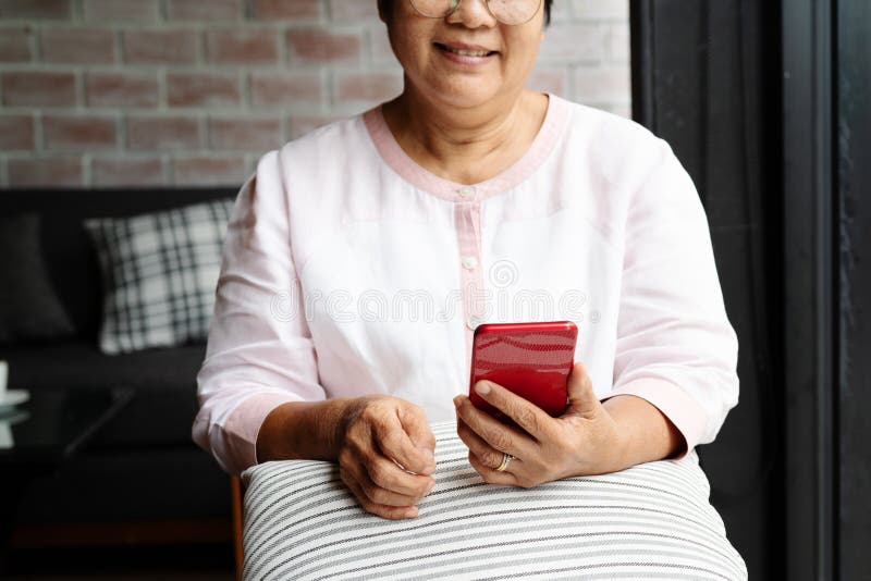 Sorrindo idosa usando celular enquanto se senta no sofá em casa imagens de stock Sorrindo idosa usando celular enquanto se senta no sofá em casa imagens de stock
