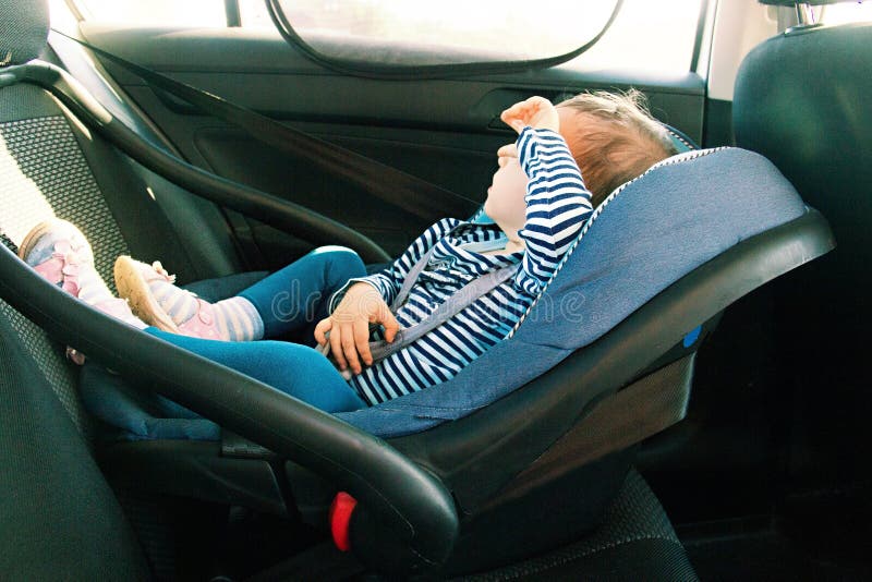 Sorriso del bambino in una sede di automobile di sicurezza obbligazione la ragazza di un anno del bambino nell'usura blu si siede fotografia stock libera da diritti Sorriso del bambino in una sede di automobile di sicurezza obbligazione la ragazza di un anno del bambino nell'usura blu si siede fotografia stock libera da diritti