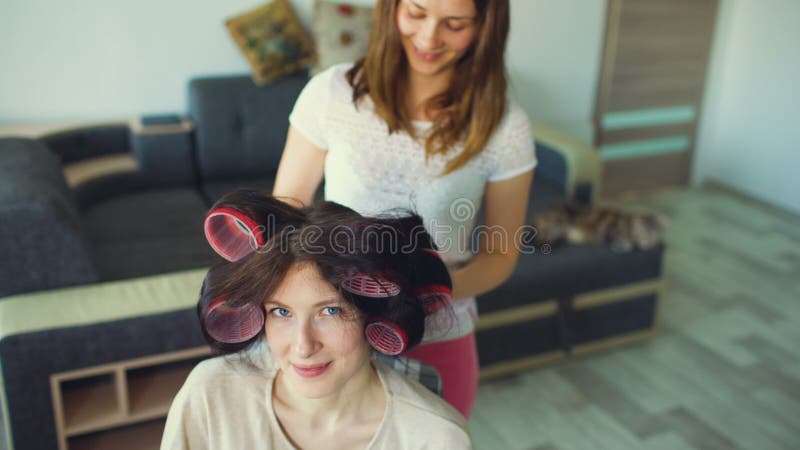 Sorriso engraçado da mulher quando seu girlfrind fizer o penteado do encrespador do divertimento