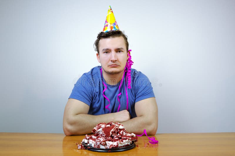 Sorrorful man with birthday party cone hat on head and crumple cake, crying. guy in bad mood while having celebration stock image Sorrorful man with birthday party cone hat on head and crumple cake, crying. guy in bad mood while having celebration stock image