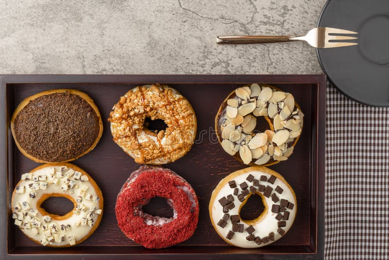 Sortiment av donuts på trämagasinet med den mörka plattan och liten gaffel och servett arkivfoton Sortiment av donuts på trämagasinet med den mörka plattan och liten gaffel och servett arkivfoton
