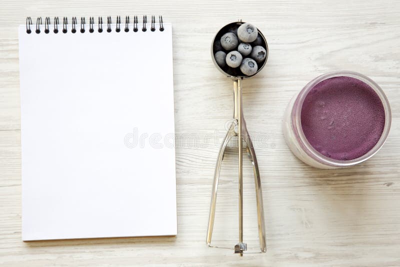 Sorvete do gelado do mirtilo no frasco plástico, na colher do gelado com mirtilos congelados e no bloco de notas em um fundo de m imagem de stock Sorvete do gelado do mirtilo no frasco plástico, na colher do gelado com mirtilos congelados e no bloco de notas em um fundo de m imagem de stock