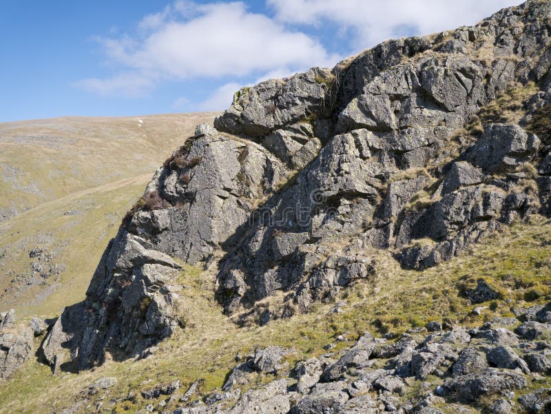 Against a blue sky, an igneous rock outcrop near Comb Crags, Birk Side, near Helvellyn in the Lake District National Park, Cumbria, England, UK. Against a blue sky, an igneous rock outcrop near Comb Crags, Birk Side, near Helvellyn in the Lake District National Park, Cumbria, England, UK