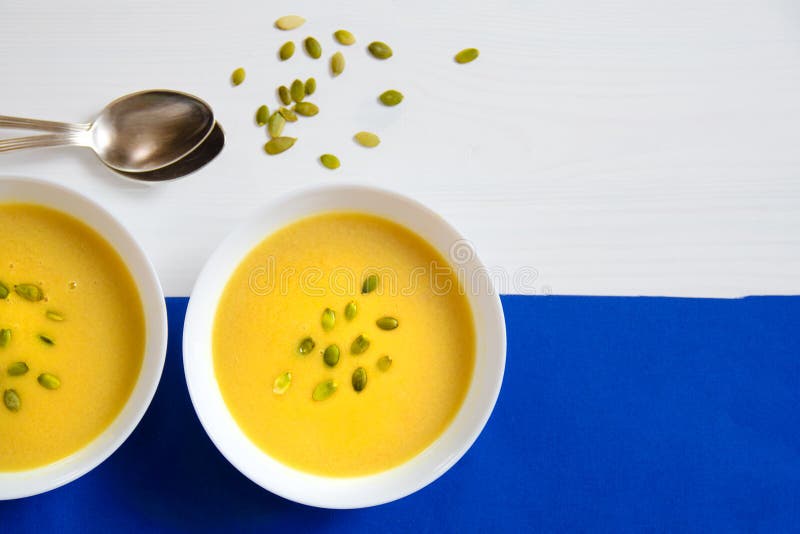 Soup of pumpkin and sunflower seeds in a white plate with silver spoons on a bright background. The concept of healthy eating