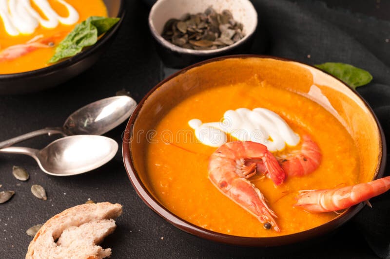 Soupe avec des crevettes, des graines de citrouille dans des cuvettes foncées et des cuillères d'argent image stock Soupe avec des crevettes, des graines de citrouille dans des cuvettes foncées et des cuillères d'argent image stock