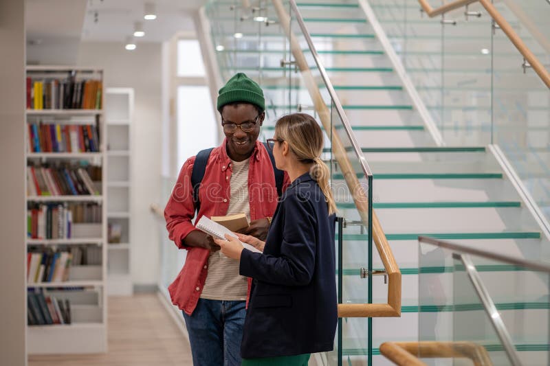 Sourire africain américain gars communication avec la petite amie européenne dans la bibliothèque universitaire images stock