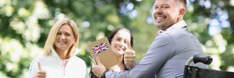 Sourire homme handicapé en fauteuil roulant étudier l'anglais avec des amis et montrer le signe du pouce images stock