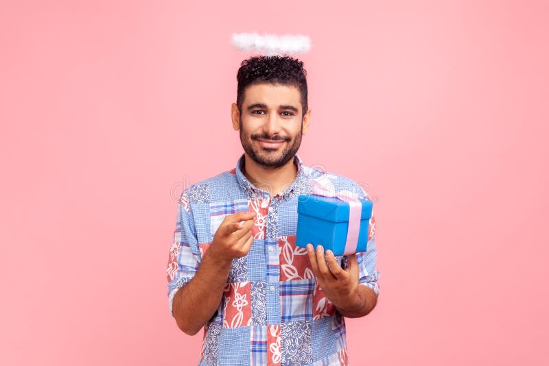 Sourire mignon homme barbu angélique avec nimb sur la tête tenant boîte cadeau et pointant vers la caméra vous choisissant de donn photos stock