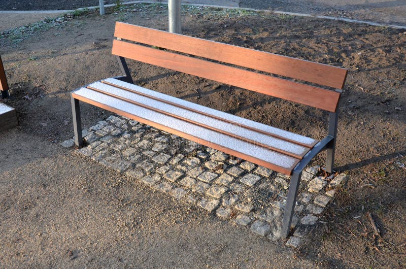 Sous le banc sont des rectangles en tuiles. sinon la surface molle de la trajectoire compactée du parc de gravier pourrait éroder. autrement, la surface molle de la trajectoire compactée du parc de gravier pourrait éroder les chaussures par abrasion. assis à côté d'une petite chapelle avec des bancs de bois glacé.