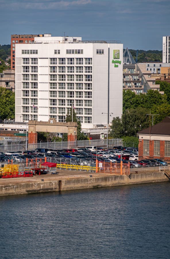 Southampton, England, UK - July 7, 2022: Harbor scenery. White Holiday Inn building near port behind parking lot under blue sky. Quay up front. Southampton, England, UK - July 7, 2022: Harbor scenery. White Holiday Inn building near port behind parking lot under blue sky. Quay up front