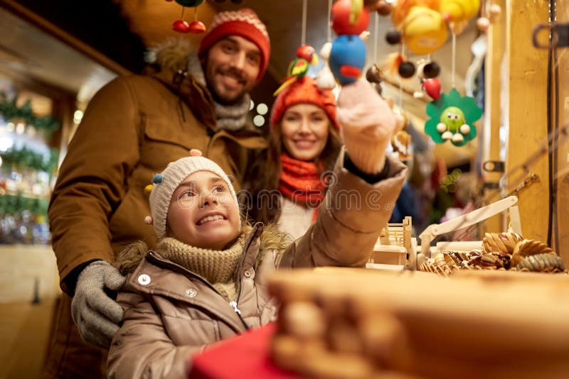 Family, winter holidays and celebration concept - happy mother, father and little daughter choosing souvenirs at christmas market on town hall square in tallinn, estonia. Family, winter holidays and celebration concept - happy mother, father and little daughter choosing souvenirs at christmas market on town hall square in tallinn, estonia