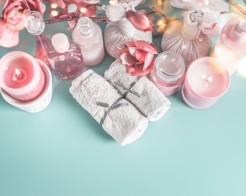 Spa and beauty cosmetic on blue desktop background with towels, candle and pink flowers. Top view