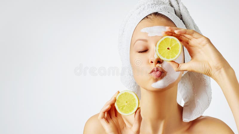 Cosmetology, skin care, face treatment, spa and natural beauty concept. Woman with facial mask holds lemon, over white background with copy space. Cosmetology, skin care, face treatment, spa and natural beauty concept. Woman with facial mask holds lemon, over white background with copy space