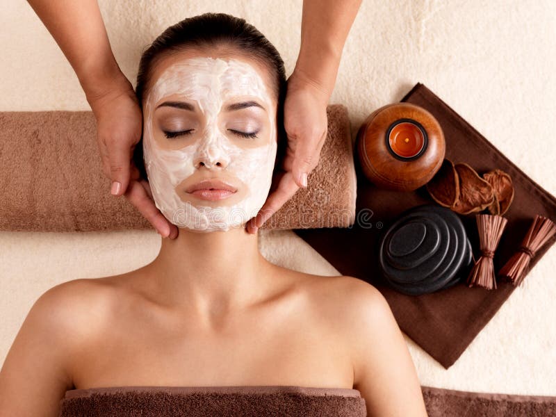 Spa massage for young woman with facial mask on face - indoors. Spa massage for young woman with facial mask on face - indoors