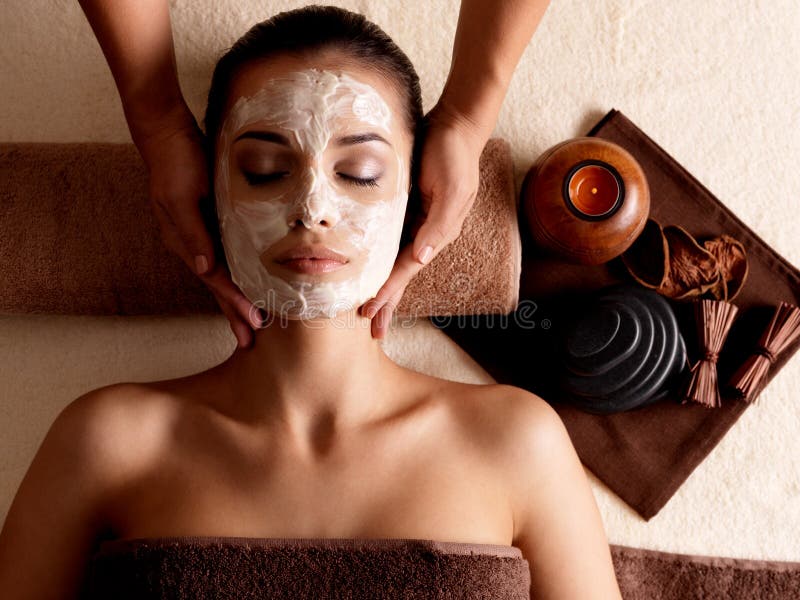 Spa massage for young woman with facial mask on face - indoors. Spa massage for young woman with facial mask on face - indoors