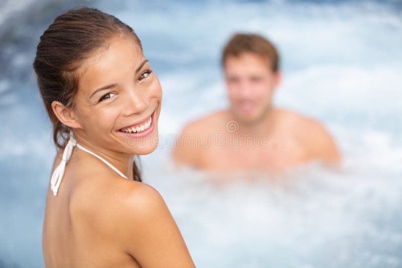 Spa resort jacuzzi hot tub couple, women and man. Girl enjoying water in outdoor whirlpool smiling happy at camera during relaxing vacation holidays retreat. Multiethniic young couple, Asian woman. Spa resort jacuzzi hot tub couple, women and man. Girl enjoying water in outdoor whirlpool smiling happy at camera during relaxing vacation holidays retreat. Multiethniic young couple, Asian woman.