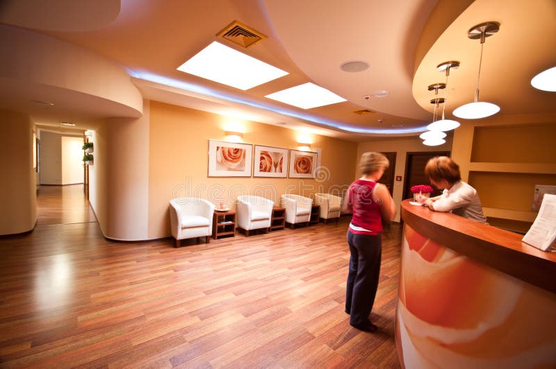 SPA waiting room. A small SPA waiting room with comfortable armchairs and reception desk. Motion blurred receptionist with customer or patient SPA waiting room. A small SPA waiting room with comfortable armchairs and reception desk. Motion blurred receptionist with customer or patient