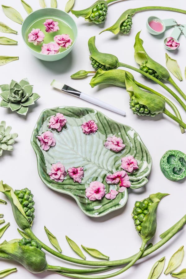 Spa or Wellness background. Bowl in shape of tropical leaf with flowers and water on white background with green leaves and calla