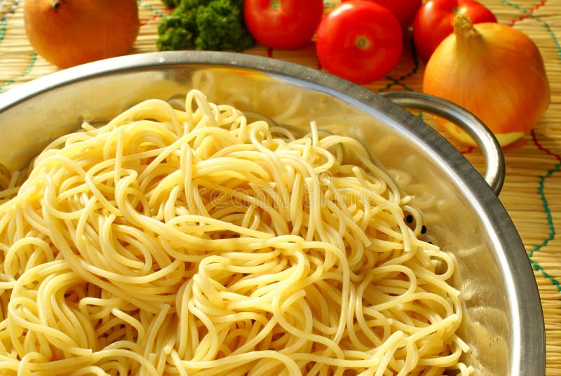 Boiled spaghetti in metal colander and vegetables prepared for making sauce