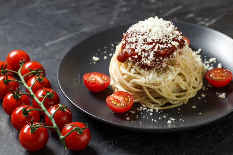 Spaghetti pasta with grated parmesan cheese and cherry tomatoes, on dark background, Italian dish