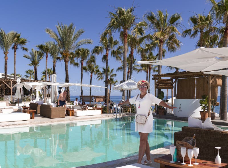 A pretty woman in a white dress is standing near the pool at Nikki Beach Club in Marbella