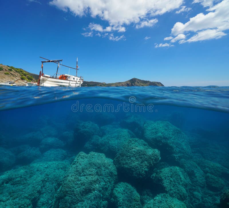 Spain Mediterranean sea a typical boat with the coastline in background and rocks underwater, split view above and below water surface, Costa Brava, Roses, Catalonia, Girona. Spain Mediterranean sea a typical boat with the coastline in background and rocks underwater, split view above and below water surface, Costa Brava, Roses, Catalonia, Girona