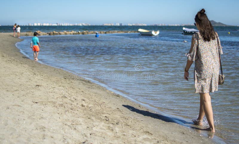 Spanien Murcia - Juni 22, 2019: Lycklig ung kvinna som bär den tillfälliga klänningen som går på stranden arkivfoto Spanien Murcia - Juni 22, 2019: Lycklig ung kvinna som bär den tillfälliga klänningen som går på stranden arkivfoto